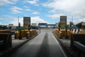 Straße mit einer Mäßstation, Absperrpfählen, Verkehrskegel, Topfpflanzen, Hinweisschilder, Straßenlaternen, Bäume und eine Brücke.