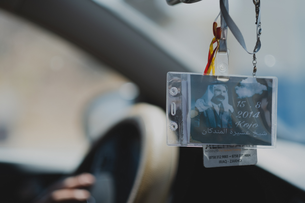 Eine Person fährt ein Auto mit einem ID-Kartenanhänger am Lenkrad, ihre Hand ist auf der linken Seite sichtbar, mit einem unscharfen Hintergrund.