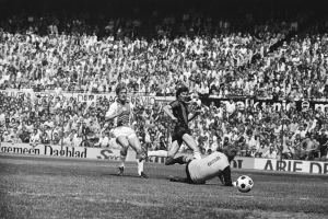 Schwarzes und weißes Foto von Männern, die auf einem Feld Fussball spielen, mit Zuschauern im Hintergrund und einem Banner mit der Aufschrift "Bundesliga 1978-79 Ajax 1-1 Hannover 96".