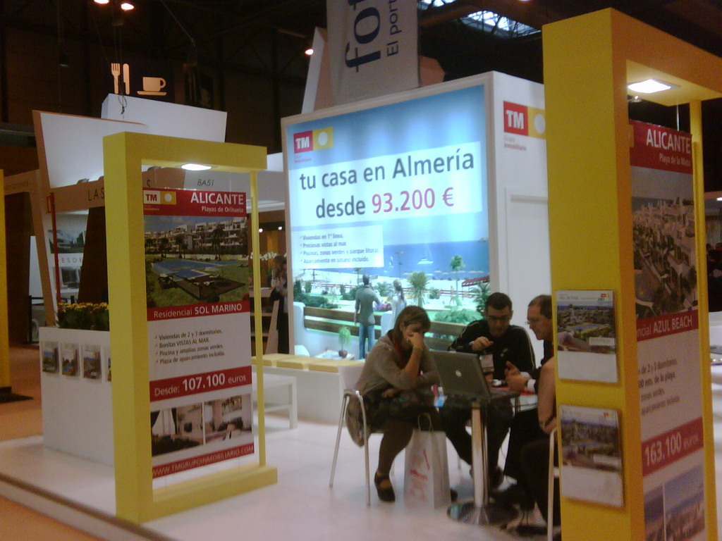 Eine Gruppe von Menschen sitzt um einen Tisch, schaut auf einen Laptop, mit verschiedenen Anzeigen auf den Flyern daneben.