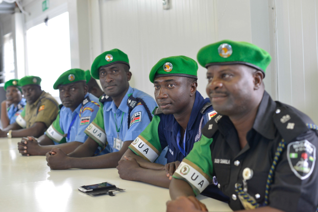 Gruppe von Polizisten, die während einer Schulung an einem Tisch sitzen, mit Mobiltelefonen und anderen Gegenständen auf dem Tisch, in einem Raum mit Fenstern und Deckenbeleuchtung.