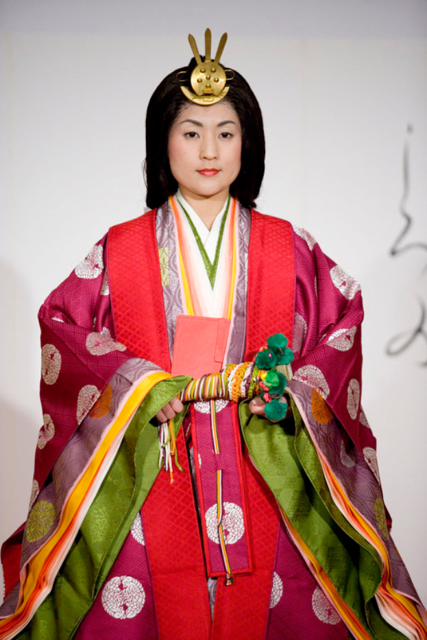 Eine Frau in einem traditionellen japanischen Kimono, mit einem leuchtend roten und grünen Kleid mit aufwändigen Mustern, steht selbstbewusst auf einem Laufsteg mit einem ordentlichen Dutt.
