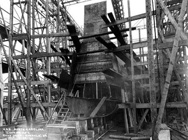 Schwarzes und weißes Foto eines Schiffs in einem Schiffbau, mit Holzpfählen und Treppen im Vordergrund und Himmel im Hintergrund, mit dem Text "Marine-Waffensysteme" in der linken unteren Ecke.