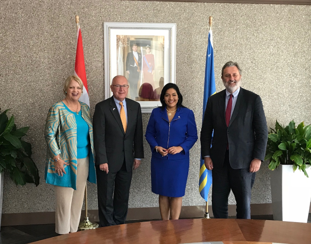 Eine Gruppe strahlender Menschen um einen Tisch mit Papieren herumstehend, umgeben von Fahnen, Topfpflanzen und einem Foto auf der Wand, feiert die Unterzeichnung eines Memorandums von Verständigung zwischen den Vereinigten Staaten und Kanada.