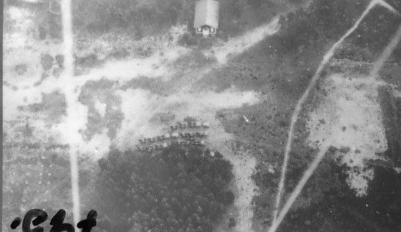 Schwarzes und weißes Foto eines Flugzeugs, das über ein Feld mit einem Gebäude im Hintergrund fliegt, mit der Beschriftung "Weltkrieg II US Air Force" unten.