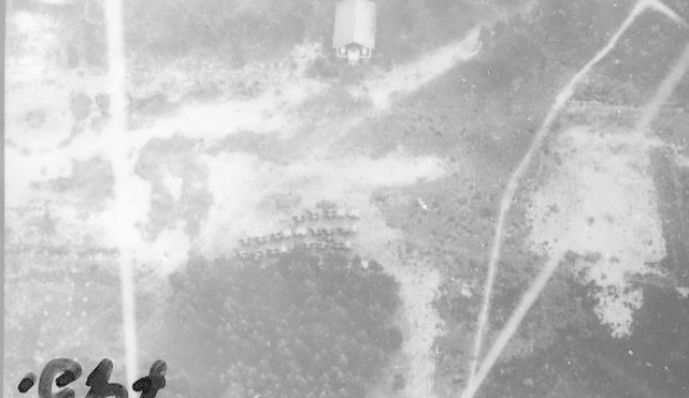 Schwarzes und weißes Foto eines Flugzeugs, das über ein Feld mit einem Gebäude im Hintergrund fliegt, mit der Beschriftung "Weltkrieg II US Air Force" unten.
