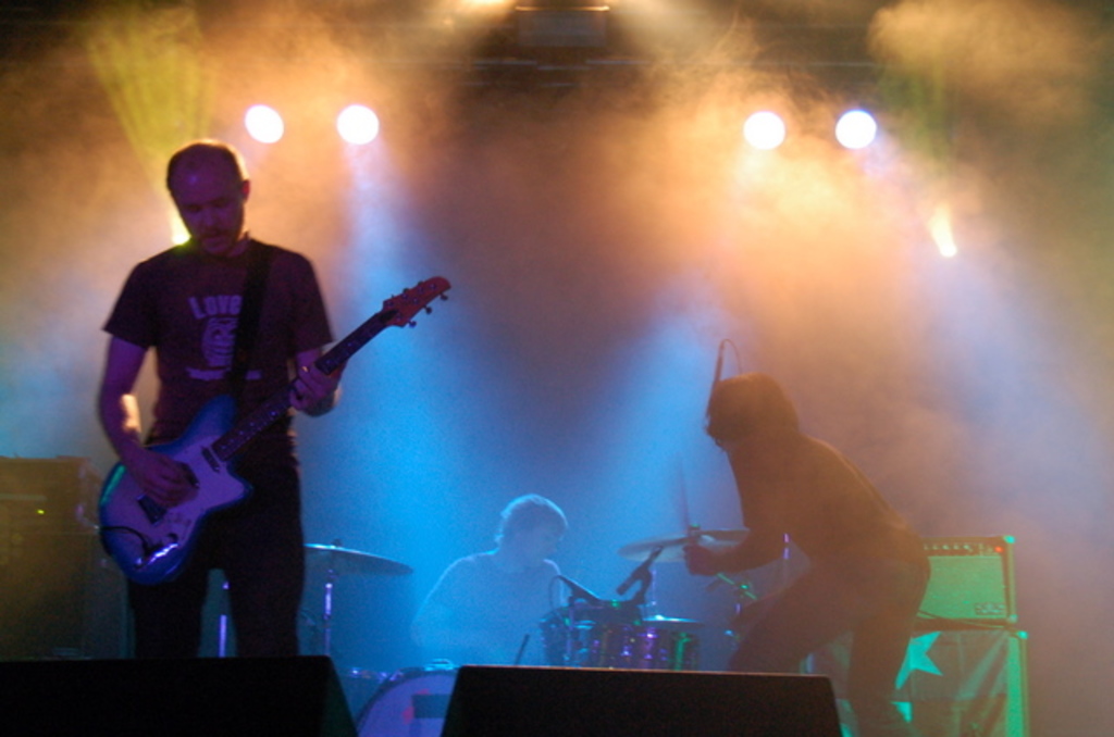 Ein musikalisches Konzert mit Lichtern oben, Musikern, die Instrumente spielen, in der Mitte und Lautsprechern auf beiden Seiten.