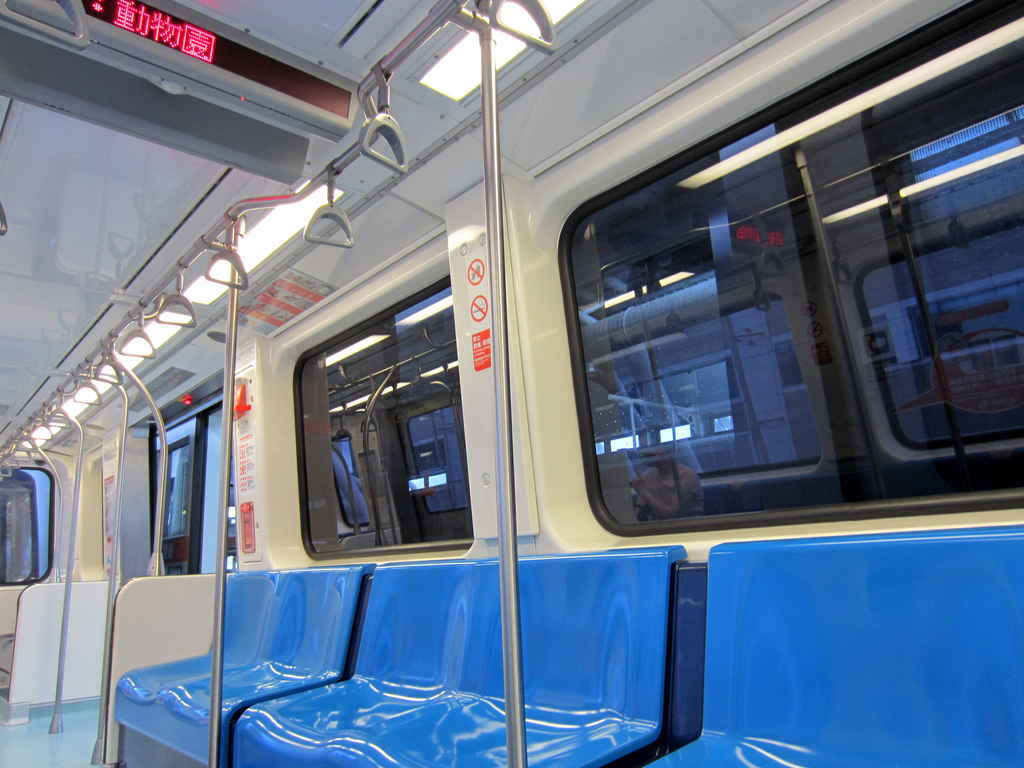 Der Innenraum eines Zuges mit Stühlen unten, Fenstern in der Mitte und einer Anzeigetafel oben.