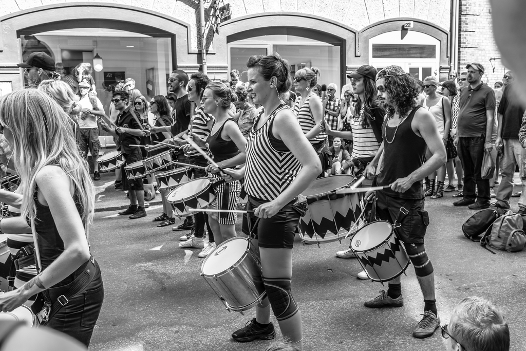 Eine Gruppe von Menschen, die draußen Musikinstrumente spielen, mit einer geschlossenen Glastür und einer Lampe im Hintergrund.