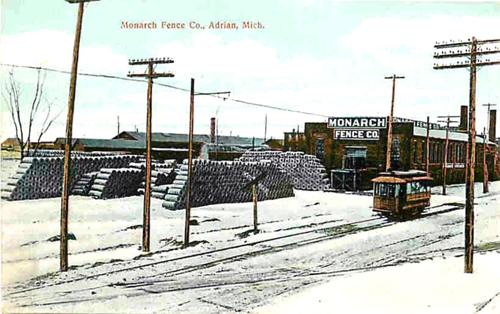 Eine schneebedeckte Landschaft mit einem Fahrzeug auf einer Spur, umgeben von Pfählen, und einer Sammlung von Gegenständen hinter den Pfählen sowie einem Fabrikgebäude im Vordergrund.