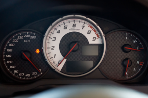 Nahaufnahme eines Autodashboards mit Tachometer auf schwarzem Hintergrund, weißen Zahlen und roter Nadel, die die aktuelle Geschwindigkeit anzeigt.