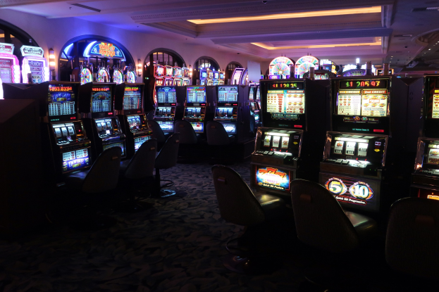 Eine Reihe von Spielautomaten zum Verkauf in einem Casino, jeder mit Text und Zahlen angezeigt, unter Deckenlampen mit Stühlen auf dem Boden.
