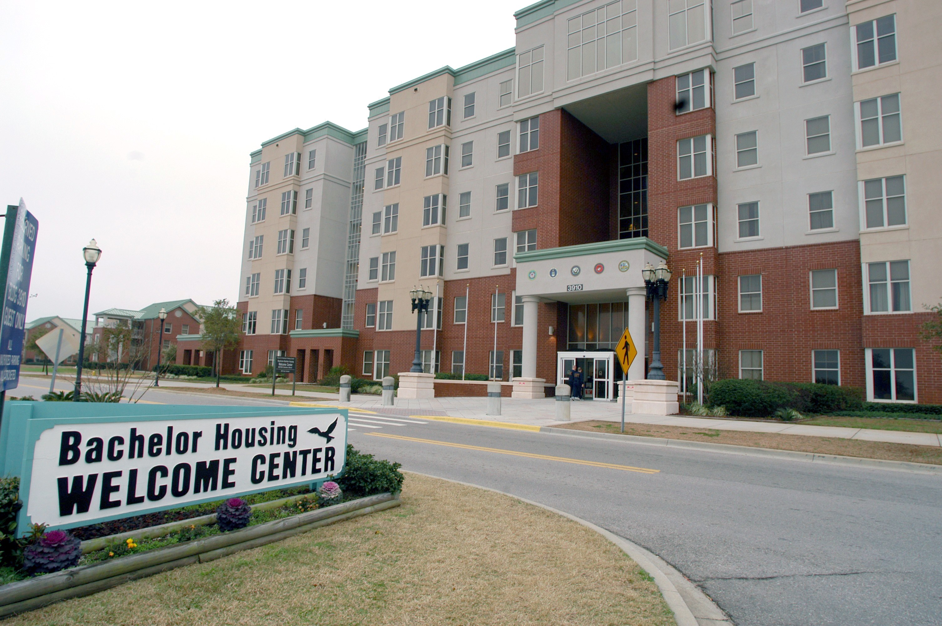 Außenansicht eines Bachelor-Housing-Willkommenszentrums mit Gebäuden, Straßeninfrastruktur, Fahrzeugen, Grünflächen und einem klaren Himmel.