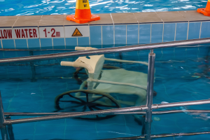 Schwimmbad mit einem Stuhl in der Mitte, umgeben von Sicherheitskegeln und einem Geländer, mit einer Wandtafel, auf der verfügbare Schwimmausrüstung angezeigt wird.