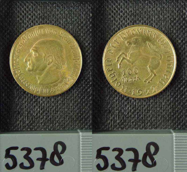 Zwei Goldmünzen aus Deutschland im Jahr 1922, jeweils mit einem Nennwert von 100 Mark, werden auf einer schwarzen Oberfläche mit Zahlen unten platziert.