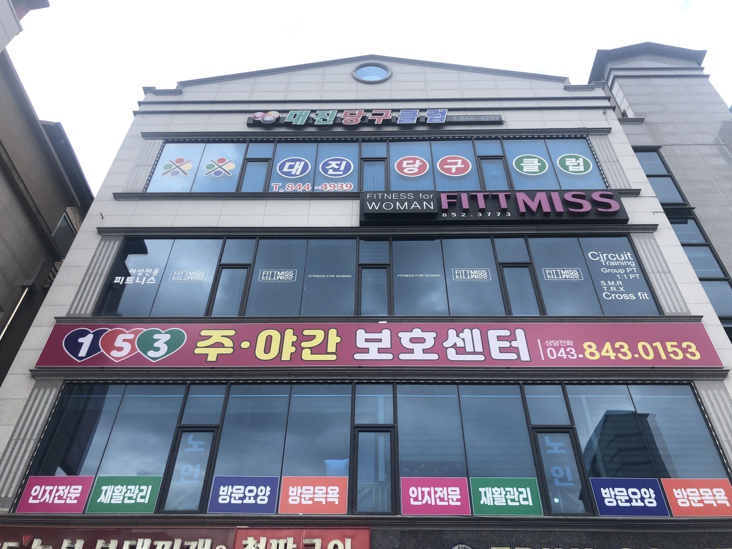 Ein Gebäude in Seoul, Südkorea, mit einem Schild, auf dem "Fitness für Frau" steht, Fenstern und Texttafeln vor einem Himmelhintergrund.