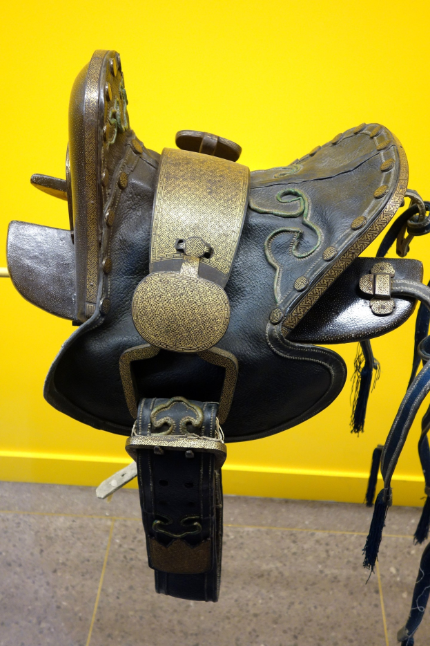 Nahaufnahme eines Pferdesattels, der auf einem Regal in einem Geschäft gegen eine gelbe Wand gestellt ist.