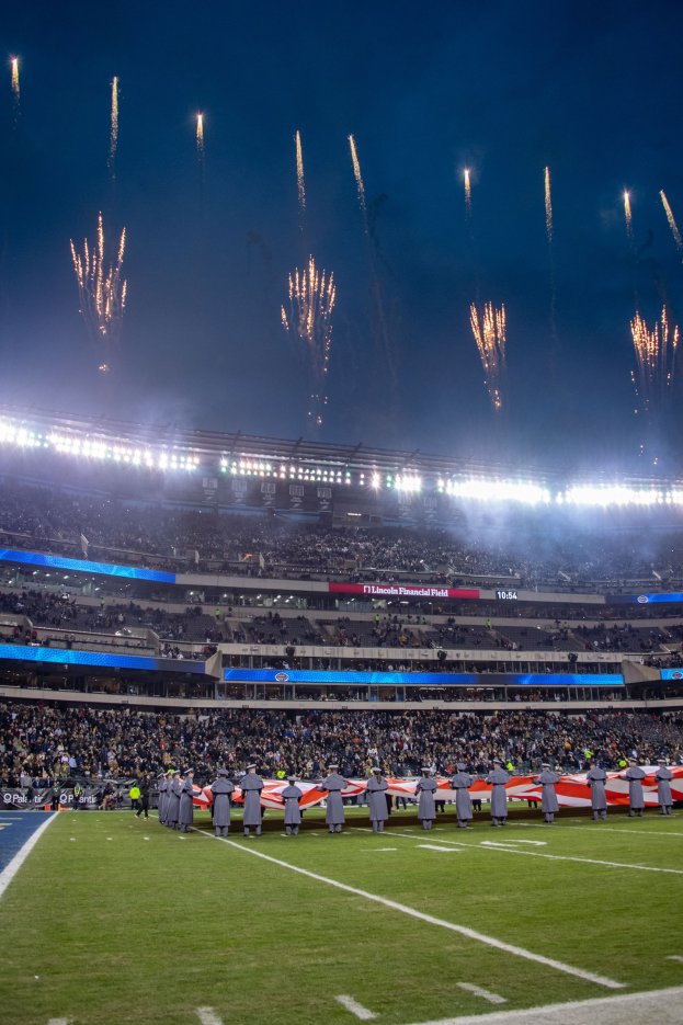 Ein Fußballstadion voller Zuschauer unter hellen Lichtern, mit Feuerwerk, das in der Nacht über dem Himmel explodiert.