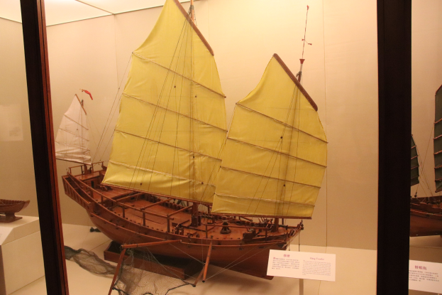 Holzmodell eines Segelboots in einer Glasvitrine mit Informationsschildern im Hintergrund.