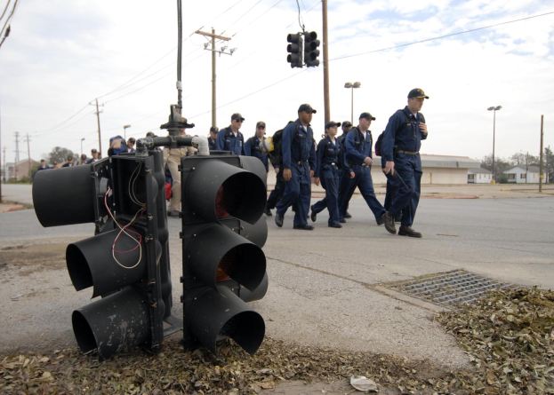 Gruppe von Polizisten in Uniform, die eine Straße mit Strommasten und Gebäuden entlanggehen unter einem klaren blauen Himmel.