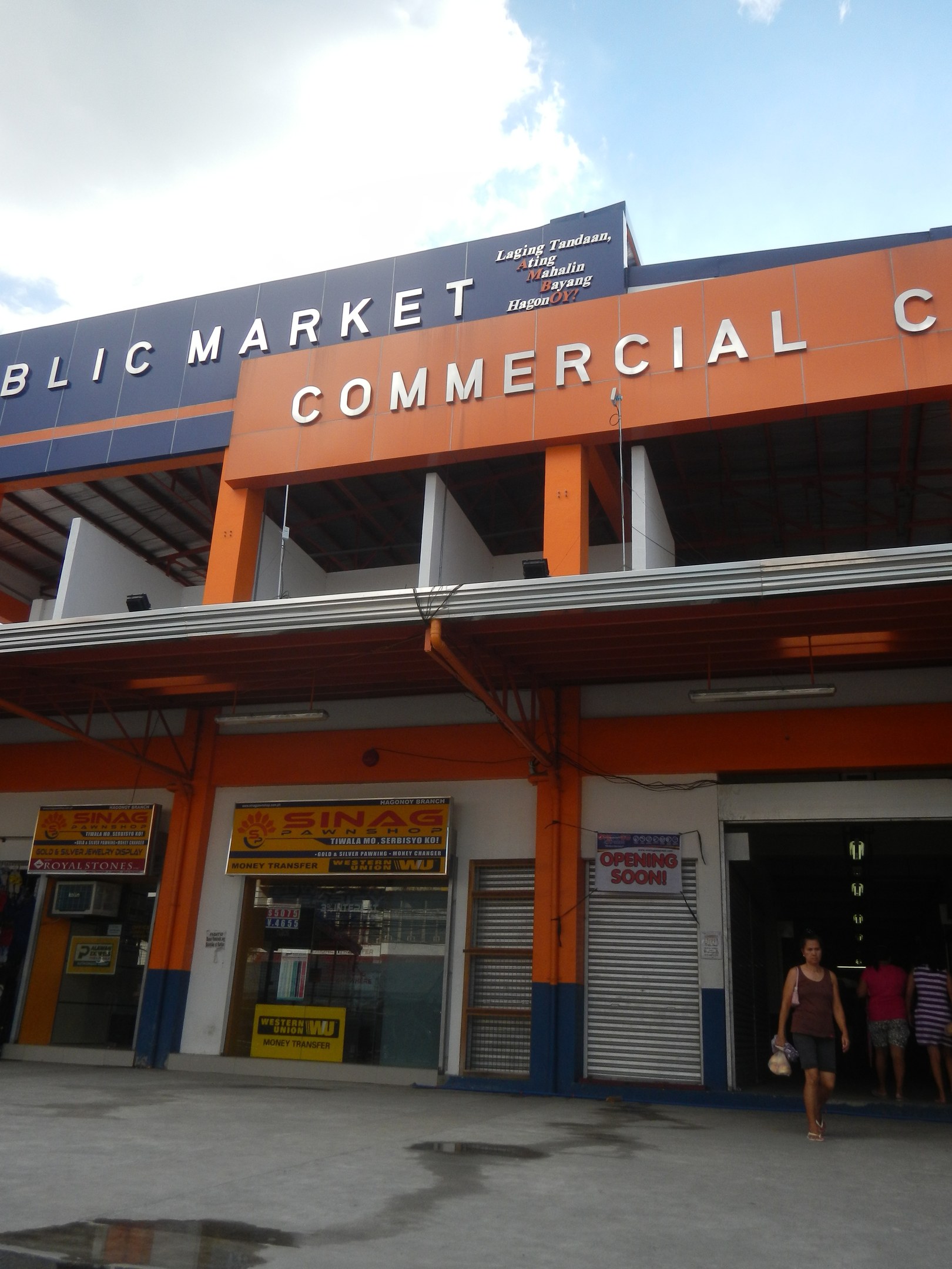 Öffentlicher Marktkomplex mit Menschen vor dem Gebäude, Text auf dem Gebäude und sichtbarem Himmel.