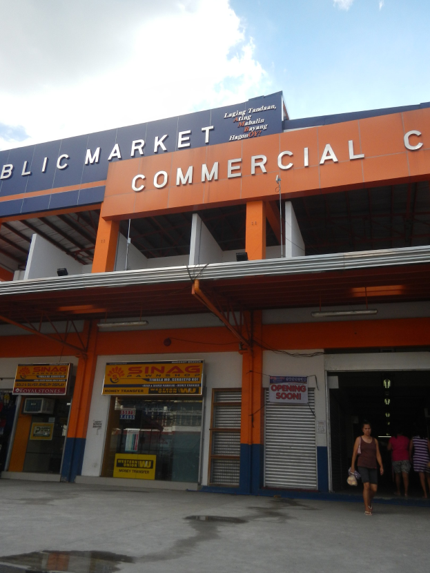 Öffentlicher Marktkomplex mit Menschen vor dem Gebäude, Text auf dem Gebäude und sichtbarem Himmel.