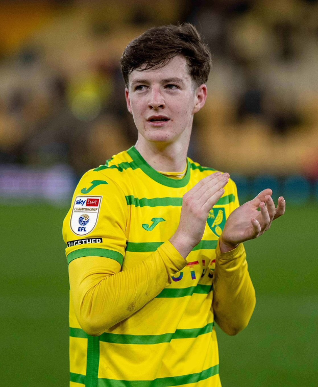 Ein junger Mann in einem gelb-grünen T-Shirt klatscht auf einem Fußballfeld jubelnd in die Hände, mit einem unscharfen Hintergrund, der seine freudige Reaktion auf das erzielte Tor betont.