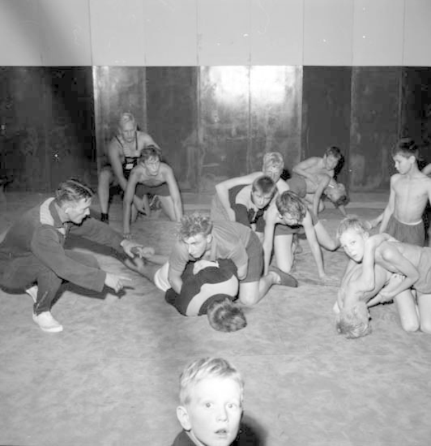 Schwarz-weißes Bild von jungen Jungs, die in einem Gymnastikraum kämpfen, mit einer Wand im Hintergrund.
