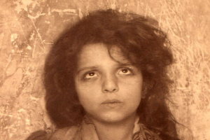 Ein Schwarz-Weiß-Foto eines jungen Mädchens mit langen Locken, das angeblich die Tochter eines großen Diktators ist, mit einer Wand im Hintergrund und einem Wasserzeichen in der rechten unteren Ecke.