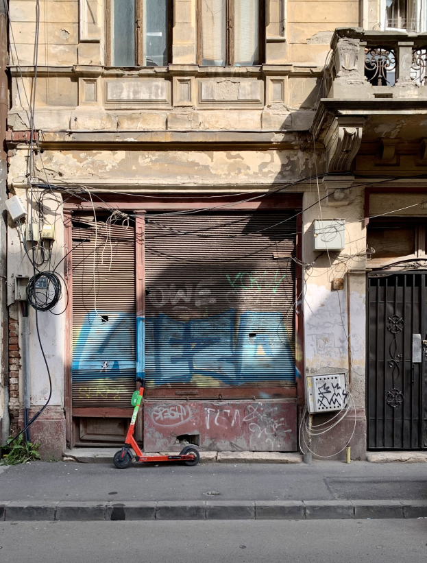 Ein roter Roller, der auf einer Straße neben einem Gebäude mit Fenstern, Läden und einem Tor geparkt ist, mit sichtbaren Kabeln und Straßenobjekten.