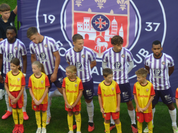 Gruppe junger Menschen auf einem Fußballfeld mit einem Banner im Hintergrund, auf dem "Preston Primary School Football Team" steht.