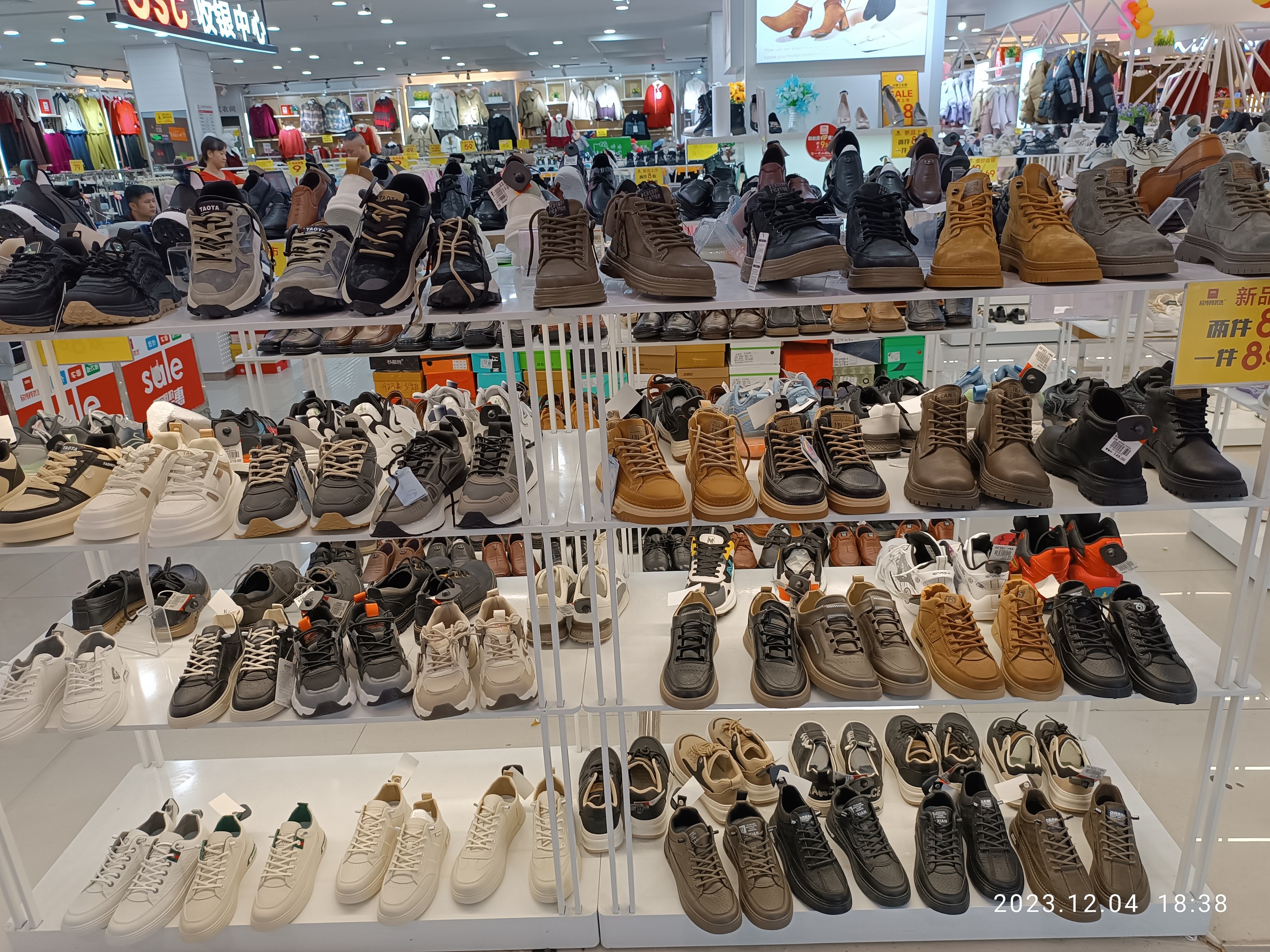 Ein Schuhgeschäftsinnenraum mit verschiedenen Schuhen auf Ständern, Preisetiketten sichtbar, Menschen im Hintergrund, Kleiderauslagen, Deckenbeleuchtung, ein Bildschirm und ein Wasserzeichen, das einen Laden in China anzeigt.