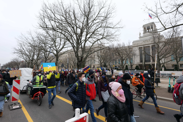 Eine große Gruppe von Menschen nimmt an einer Protestdemo in Washington, D.C. am 21. Januar 2020 teil und marschiert eine Straße entlang, wobei einige Schilder und Plakate tragen und andere Fahrräder fahren, mit Schildern, Bäumen und einem klaren blauen Himmel im Hintergrund.