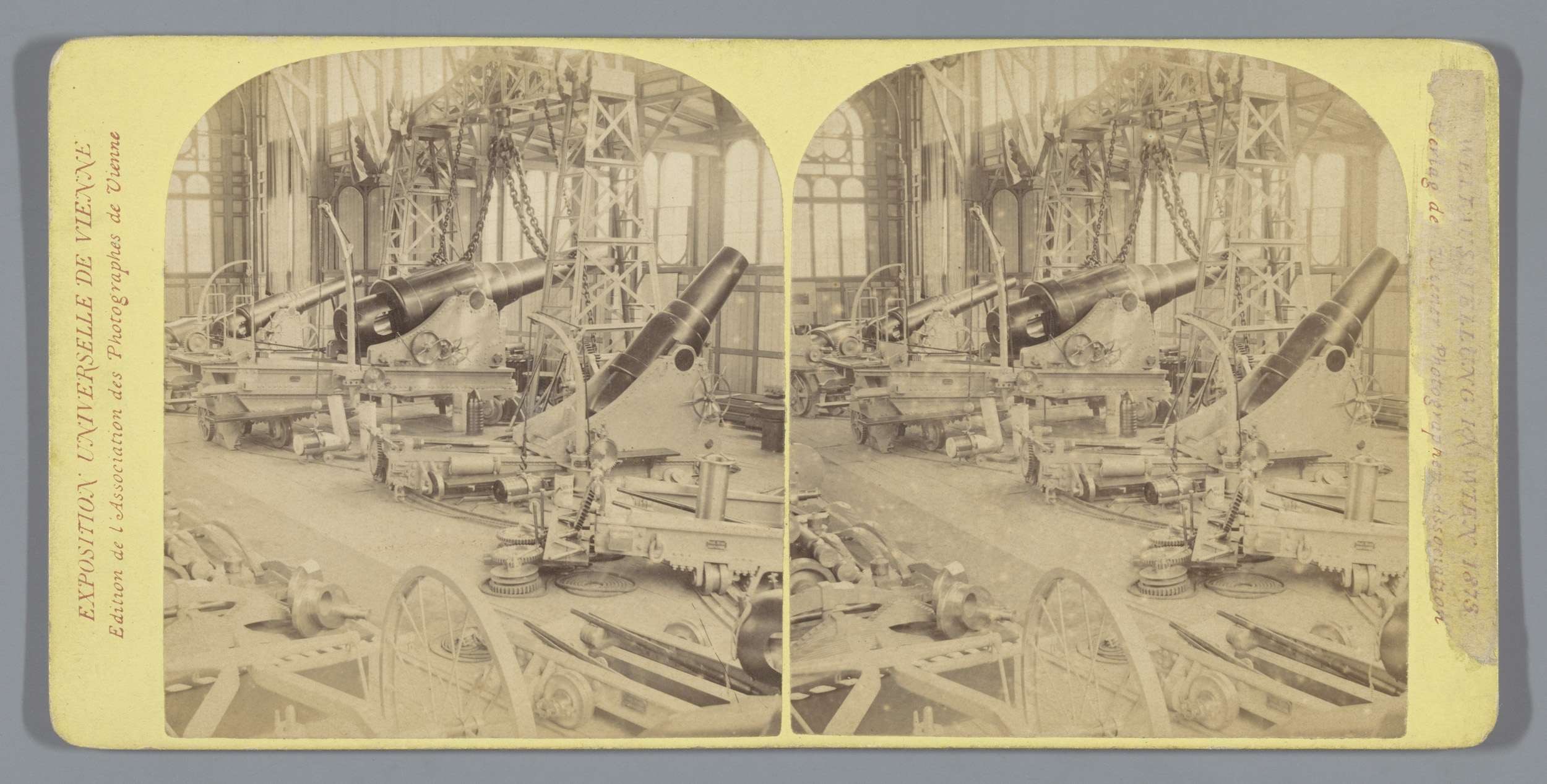 Schwarzes und weißes Foto eines alten Fabrikinneren mit einem großen Kanonen in der Mitte, umgeben von anderen Kanonen, Metallstangen und Gegenst├Ąnden auf dem Boden, mit Text auf der linken Seite.