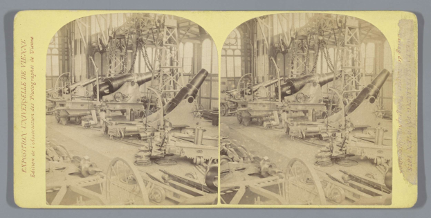 Schwarzes und weißes Foto eines alten Fabrikinneren mit einem großen Kanonen in der Mitte, umgeben von anderen Kanonen, Metallstangen und Gegenst├Ąnden auf dem Boden, mit Text auf der linken Seite.