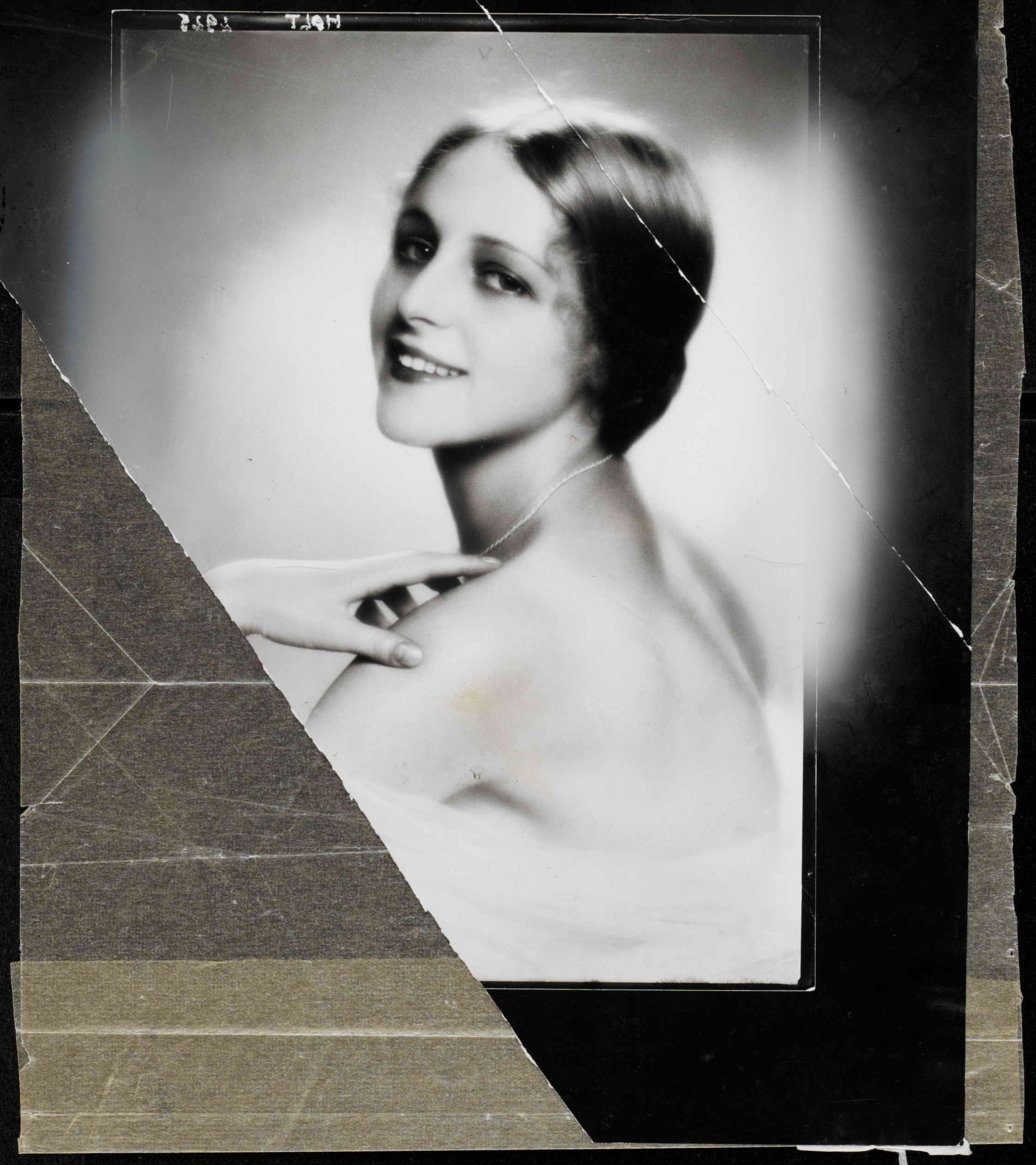 Schwarzes und weißes Porträt einer Frau in einem Kleid im 1920er-Stil mit einem ordentlichen Dutt, die warm in die Kamera lächelt.