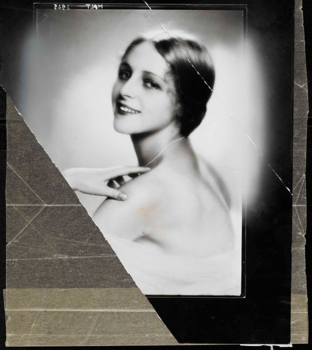 Schwarzes und weißes Porträt einer Frau in einem Kleid im 1920er-Stil mit einem ordentlichen Dutt, die warm in die Kamera lächelt.