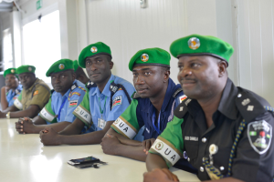 Gruppe von Polizeibeamten, die an einem Tisch während einer Schulung sitzen, mit Mobiltelefonen und anderen Gegenständen auf dem Tisch, in einem Raum mit Fenstern und Deckenleuchten.