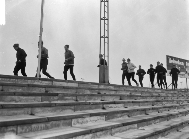 Schwarzes und weißes Foto von Menschen, die eine Treppe hochlaufen, mit einem Pfahl auf der linken Seite und einem Turm im Hintergrund.