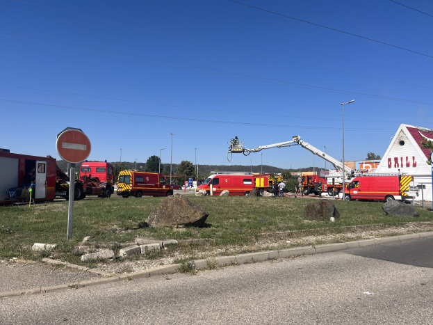 Feuerwehrl├Ąuden entlang einer Stra├če mit Trümmern und einer besch├Ądigten Tankstelle im Hintergrund unter einem bew├Âlktem Himmel.