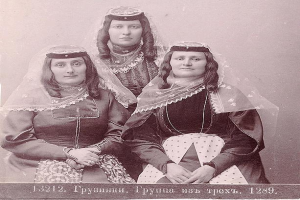 Drei Frauen in traditionellen russischen Hochzeitskleidern mit aufwendiger Stickerei und Perlen stehen vor einer weißen Wand, mit Text unten, der darauf hinweist, dass es ein russisches Hochzeitsfoto ist.