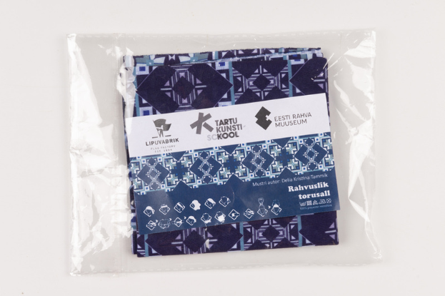 Ein blau-weiß gemustertes Stoffstück aus der Sammlung der Tartu Kunsti Skool wird in einer Plastiktüte auf einer weißen Oberfläche präsentiert, wobei ein Etikett auf dem Stoff zu sehen ist.