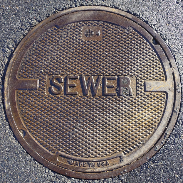 Metallschachtdeckel auf der Straße beschriftet mit 'Kanal'.