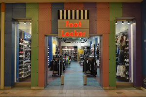 Innenansicht eines Foot Locker Schuhgeschäfts mit Kleidung an Bügeln und Regalen unter Deckenbeleuchtung, mit dem Ladengeschoss sichtbar.