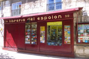 Ein zweistöckiges Gebäude mit einer Ladeneinfahrt, die ein rotes Vordach mit der Aufschrift "Libreria del Espolon" trägt, zeigt ordentlich sortierte Bücher im Inneren.