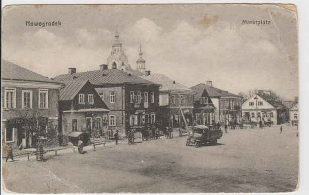 Schwarzes und weißes Foto einer Straße in Nowogrodziec, Deutschland, mit Gebäuden, Menschen, Wagen, Pfölen, Bäumen und Himmel, mit dem Text "Marktplatz in Nowogrodeek, Deutschland" oben und unten.