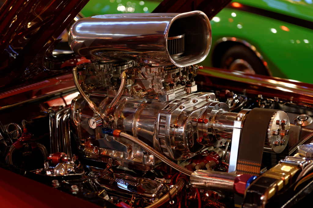 Eine Auswahl an Fahrzeugmotorteilen und anderen Komponenten mit einem im Hintergrund sichtbaren Auto.