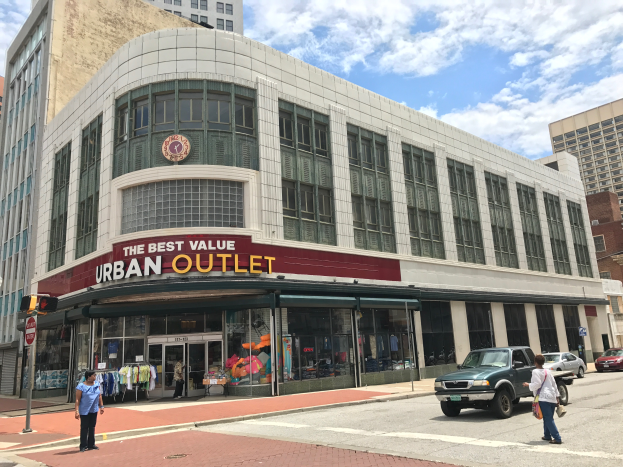 Eine belebte Stadtstraße mit Fahrzeugen und Fußgängern, hohen Glasgebäuden und einem Schild mit der Aufschrift "Der beste Preis für Stadtbewohner".