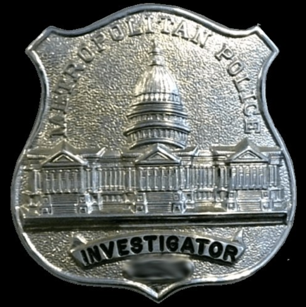 Ein silbernes Polizei-Detektivabzeichen mit der Aufschrift "Detektiv" auf einem weißen Hintergrund.