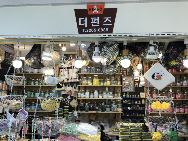 Ein Ladengeschäft mit verschiedenen Gegenständen wie Körbchen, Lichtern, Flaschen und Spielzeugen, die auf Regalen ausgebreitet sind, mit einem Schild oben, das auf einen hochbewerteten koreanischen Shop in Seoul hinweist.